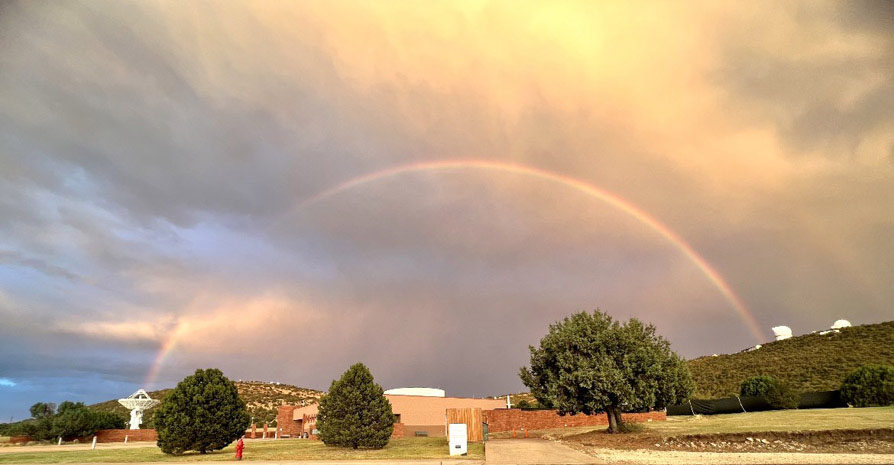 Photo shows the line of a rainbow showing through some thick clouds on a sunny day.
