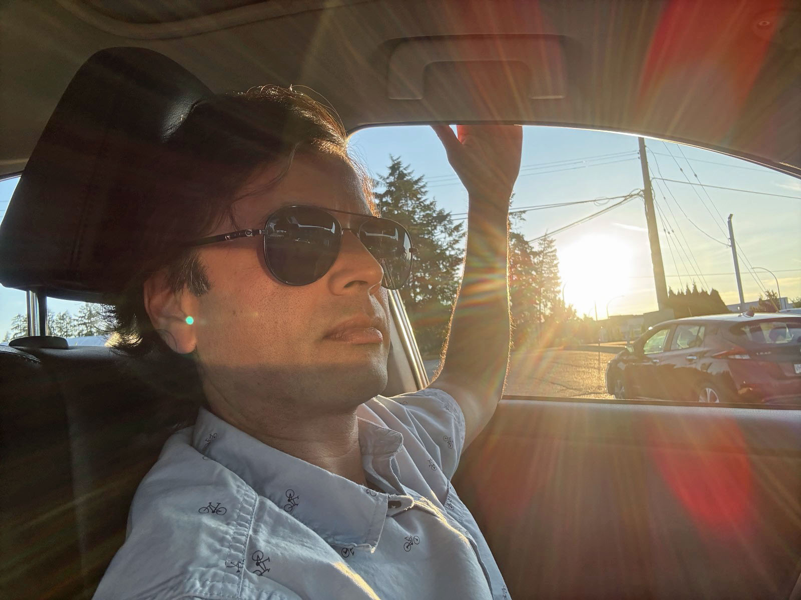 Photo of the artist in the driver's seat of a vehicle, the sun through the window casting glaring streaks of light in all directions.