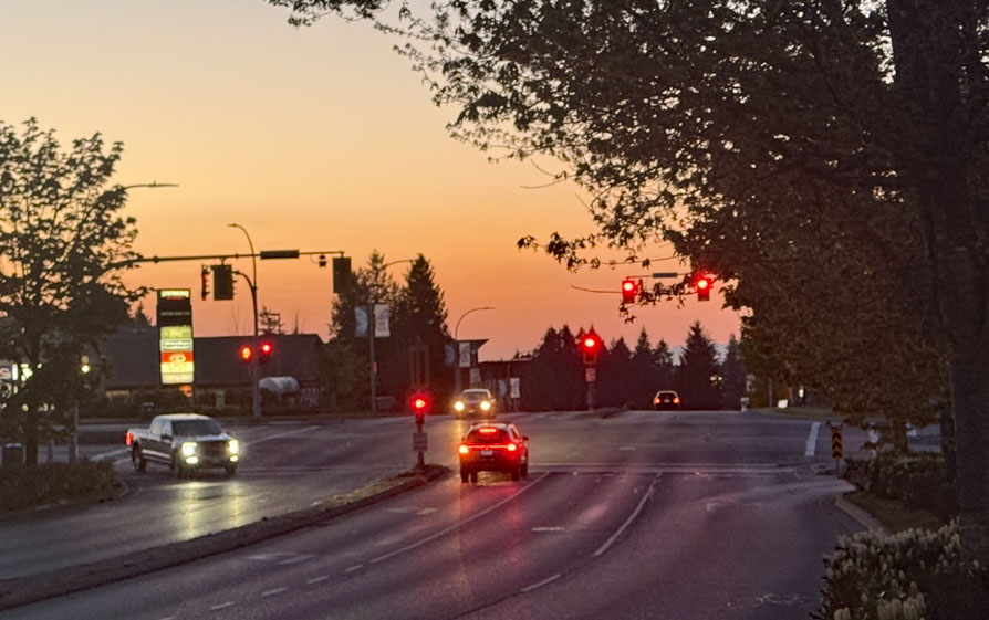 Photo of a quiet intersection early morning, car headlight and tail lights and traffic light glow brightly.